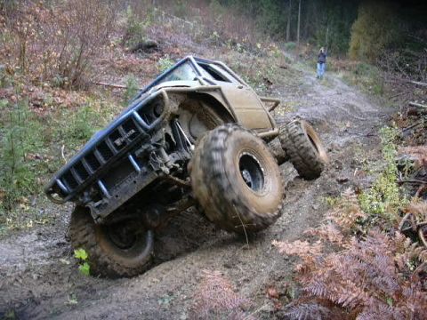 1988 Ford Bronco - Modified off-road vehicle navigates a challenging muddy terrain on a wooded trail.