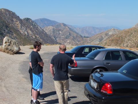 2003 Ford Crown Victoria - One man gestures while talking to another beside parked Crown Victoria sedans on a hillside overlook.
