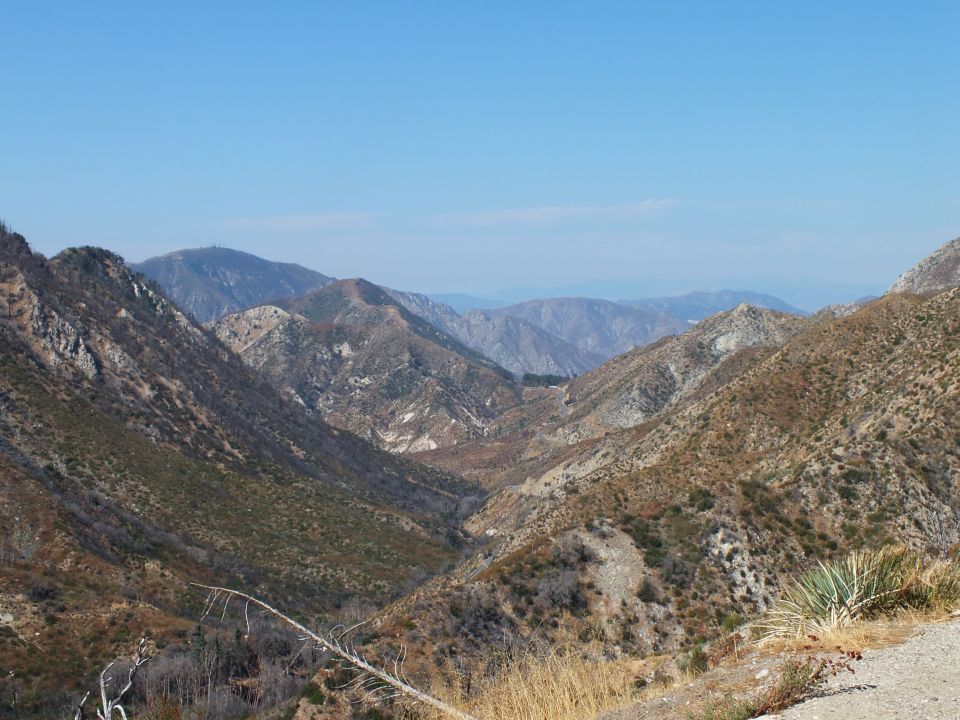 Deep mountain canyon with dry grass foreground under hazy blue sky