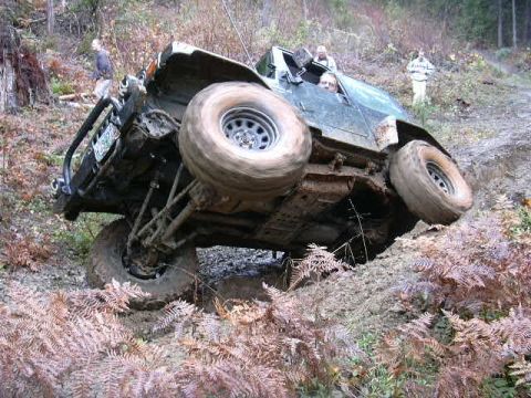 1988 Ford Bronco - An off-road vehicle is stuck on a steep, muddy incline, with its wheels off the ground.