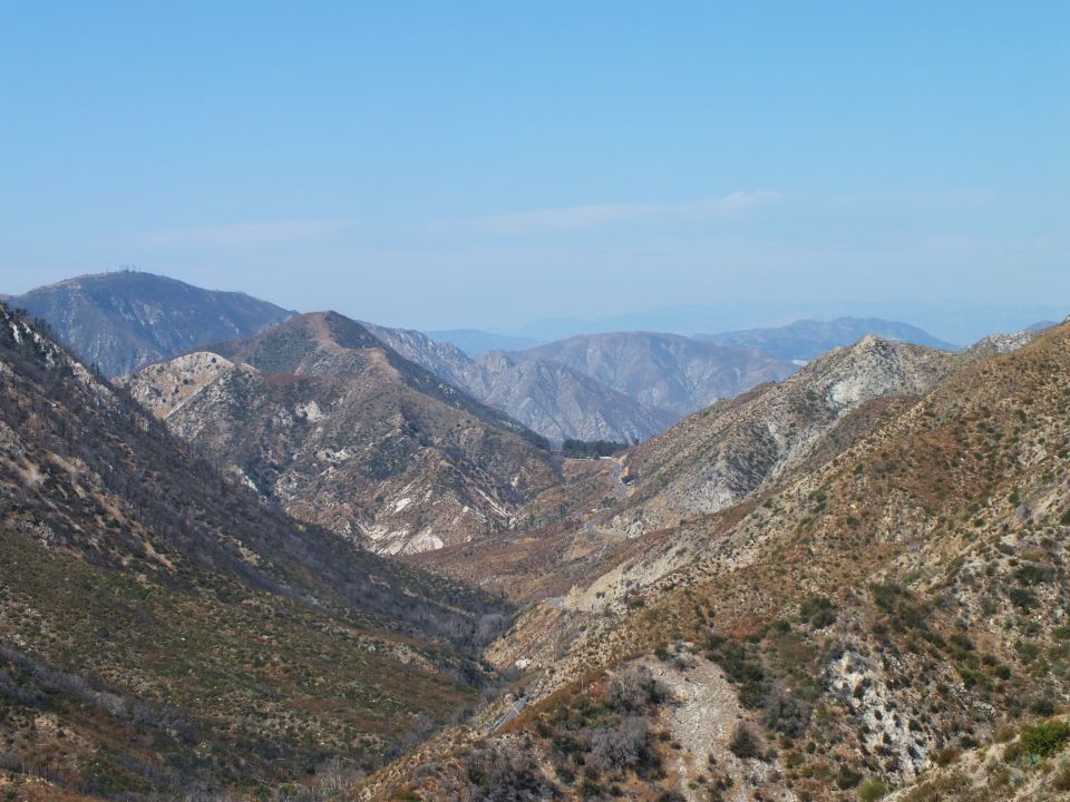 Mountain canyon descending toward distant hazy ranges under pale blue sky