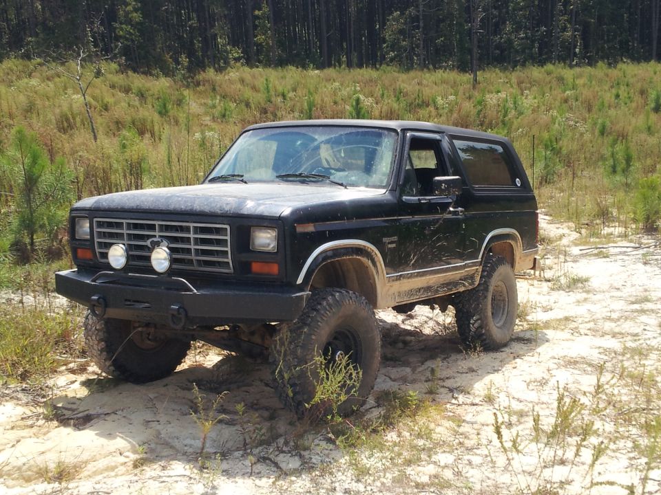 Black 1986 Ford Bronco with aftermarket bumper and off-road tires parked on sandy terrain