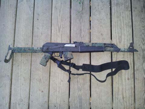 1986 Ford Bronco - Assault rifle with camouflage pattern and sling rests on a wooden deck.
