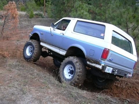 1988 Ford Bronco - Modified Ford Bronco with oversized tires navigates a steep, muddy incline.