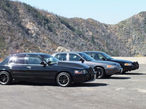 2003 Ford Crown Victoria - black sedan with chrome trim leads cars fitted with push bars on a gravel canyon lot