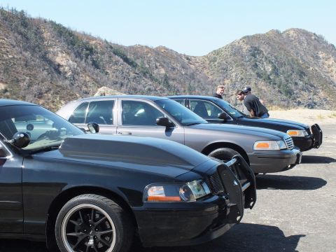 2003 Ford Crown Victoria - black sedan with grille guard sits in front of gray and black sedans on a canyon pad