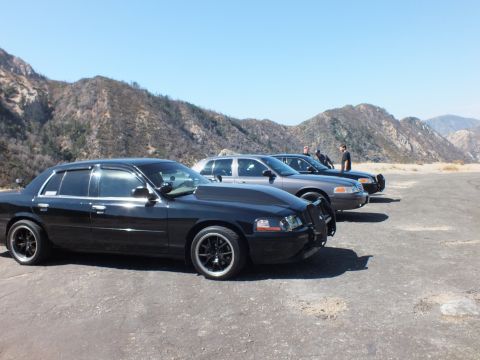 2003 Ford Crown Victoria - blacked-out sedan on dark alloys heads a line of sedans on a mountain gravel turnout