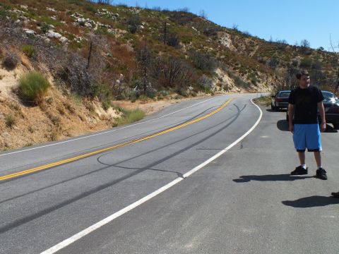 2003 Ford Crown Victoria - Person stands roadside near tire marks on a curving highway through dry hills.