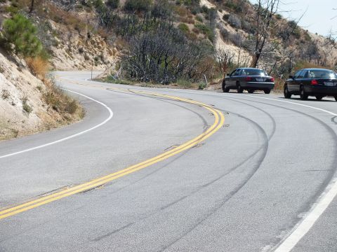2003 Ford Crown Victoria - Dark rubber streaks arc through a sweeping bend with Crown Victorias parked on the shoulder.