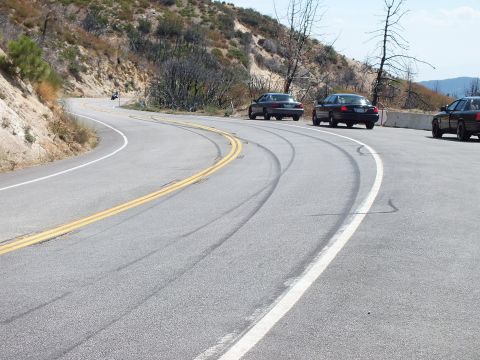 2003 Ford Crown Victoria - Tire lines follow the curve of a hillside highway lined with parked dark sedans.