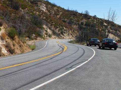 2003 Ford Crown Victoria - Winding two-lane road through dry hills, two cars pulled onto the right shoulder.