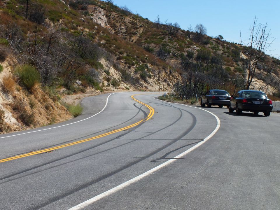 Curving mountain highway with faint tire marks and two cars parked on shoulder