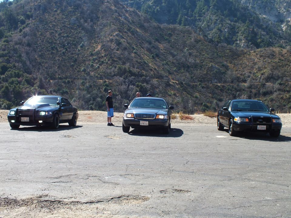 Three dark sedans parked in a dirt turnout below brushy mountain slopes