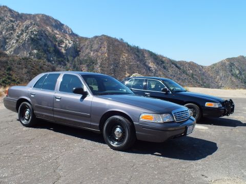 2003 Ford Crown Victoria - Gray Crown Victoria on steel wheels parked ahead of a black sedan with brush guard