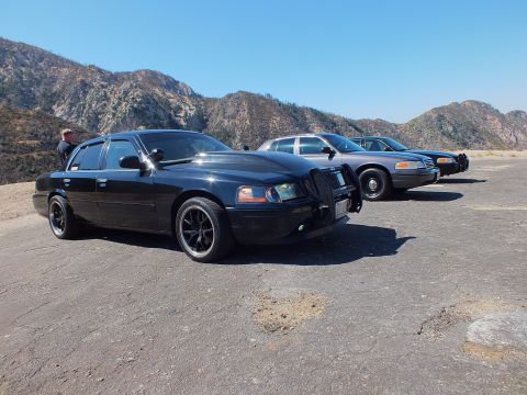 2003 Ford Crown Victoria - Three full-size sedans angled across a pullout below dry rocky mountains