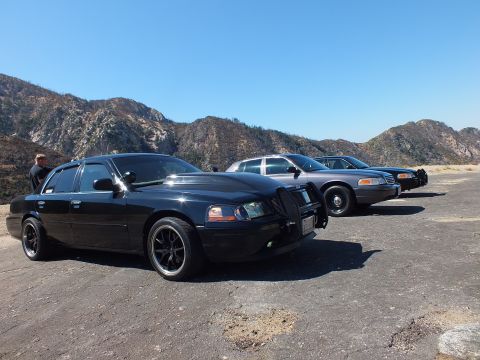 2003 Ford Crown Victoria - Lowered black Mercury leading two gray and black Ford sedans on cracked pavement
