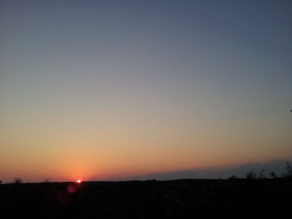 Sunset over a dark landscape with a faint lens flare. SUPERMOTORS.NET logo in the lower right