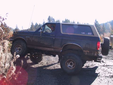 1991 Ford Bronco - A Ford Bronco navigates a muddy, off-road trail with trees in the background.