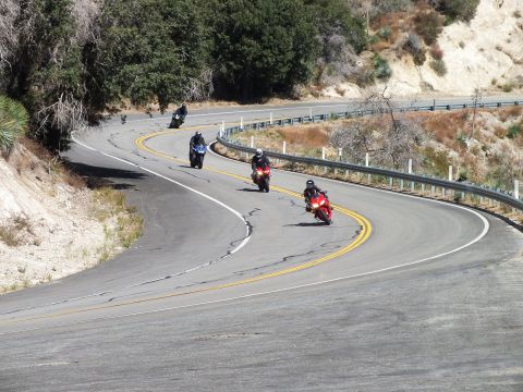 2003 Ford Crown Victoria - Several riders lean through a sweeping bend on a worn two-lane canyon highway.