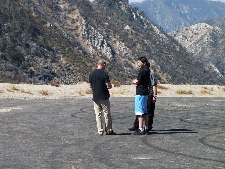 Three men talking on a dirt pullout with burned mountain ridge behind them