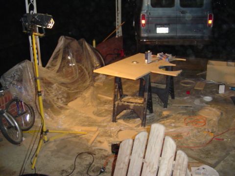1999 Ford Taurus - Cluttered nighttime garage scene with a sawhorse work table, halogen work light, bicycle, and a dark van parked at the rear.