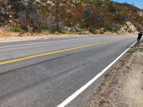 2003 Ford Crown Victoria - canyon road curves through dry chaparral hills with a figure pointing from the shoulder.