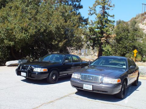 2003 Ford Crown Victoria - blacked-out police-style sedan parks next to a gray Crown Victoria with California plate 6THE144.