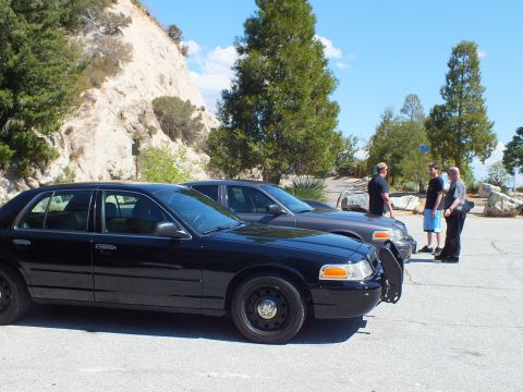 2003 Ford Crown Victoria - blacked-out Ford sedan with grille guard sits in a canyon lot as three people stand behind it.