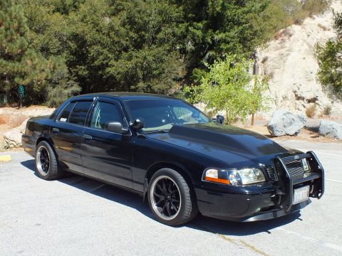 2003 Ford Crown Victoria - Front quarter of a blacked-out Ford sedan showing black wheels, billet grille, and grille guard.