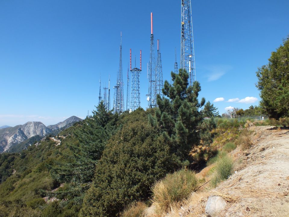 Cluster of broadcast transmission towers on a forested mountain ridge under clear blue sky