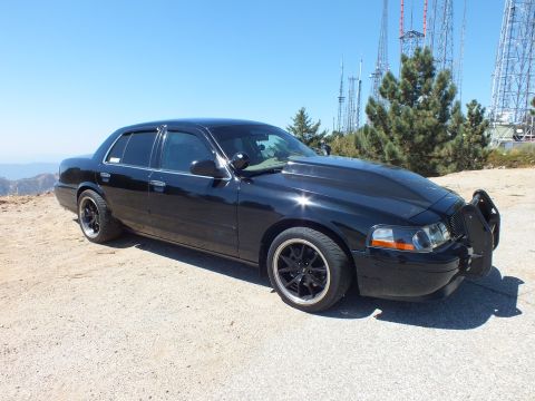 2003 Ford Crown Victoria - Profile of a lowered blacked-out Ford sedan on a dirt summit near transmission towers.