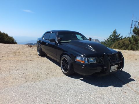 2003 Ford Crown Victoria - blacked-out Ford sedan with billet grille and push bar parked on a hazy mountaintop.