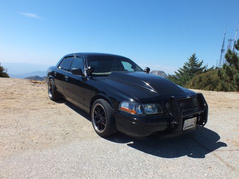 2003 Ford Crown Victoria - blacked-out full-size Ford sedan with grille guard sits on a peak above hazy valley haze.