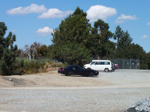 2003 Ford Crown Victoria - Black-wheeled sedan near a white minivan on a fenced gravel parking area