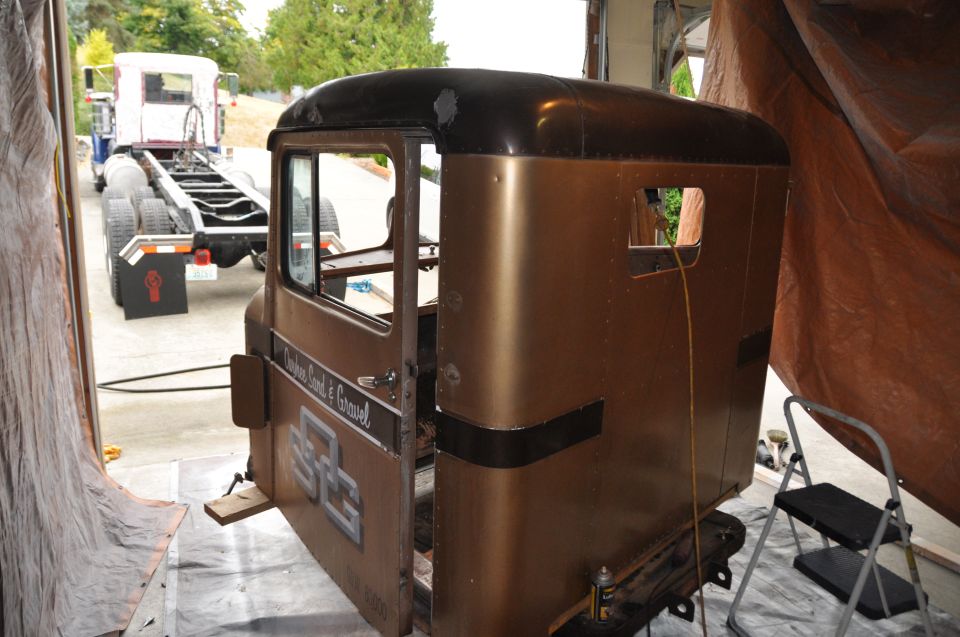 1959 Kenworth W900A cab and chassis, brown and black paint, with 'Custom Sand & Gravel' text on door. Another truck chassis is behind it