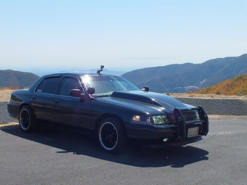2003 Ford Crown Victoria - Front-quarter view of a blacked-out police-style Ford sedan on a paved pullout