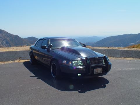 2003 Ford Crown Victoria - Lowered black Ford sedan with grille guard parked along a ridge with valley behind