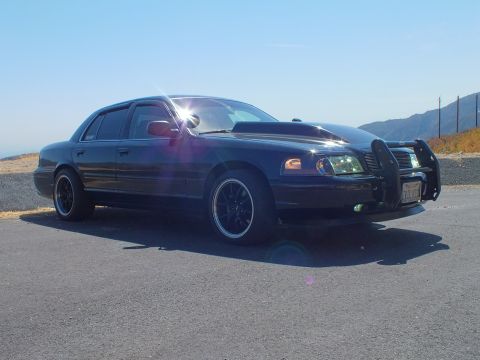2003 Ford Crown Victoria - Blacked-out Ford sedan with push bumper parked at a sunlit mountain pullout