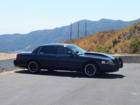 2003 Ford Crown Victoria - Profile of a lowered blacked-out police-style sedan against dry ridgelines