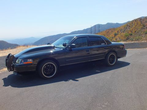 2003 Ford Crown Victoria - Side-front view of a murdered-out Ford sedan with black wheels and grille guard