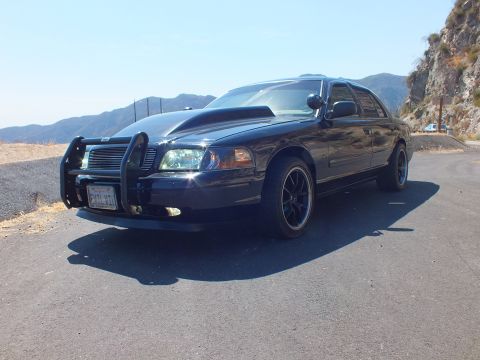 2003 Ford Crown Victoria - Front-quarter of a blacked-out police-style sedan with grille guard on a ridge road
