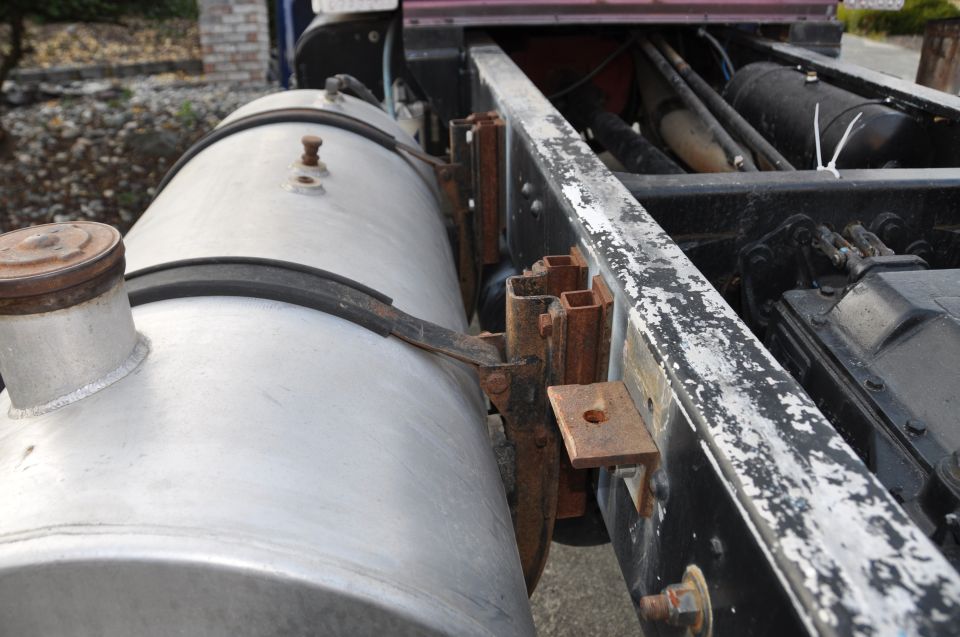 Side view of a truck's frame showing a large fuel tank and various mechanical components