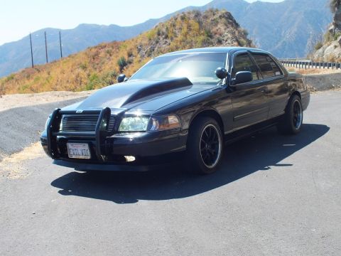 2003 Ford Crown Victoria - Blacked-out Ford sedan showing push bumper and EVIL VIC plate against dry hills