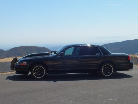 2003 Ford Crown Victoria - Lowered blacked-out Ford sedan in profile with mountains and haze behind