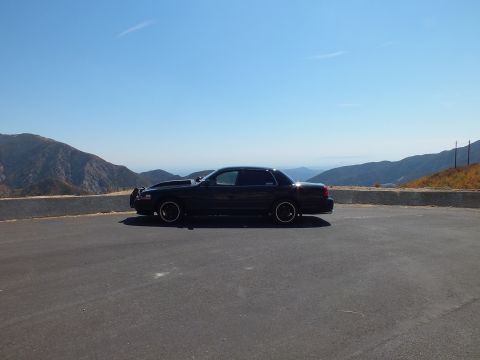 2003 Ford Crown Victoria - Distant side view of a blacked-out sedan on an empty pullout under clear blue sky