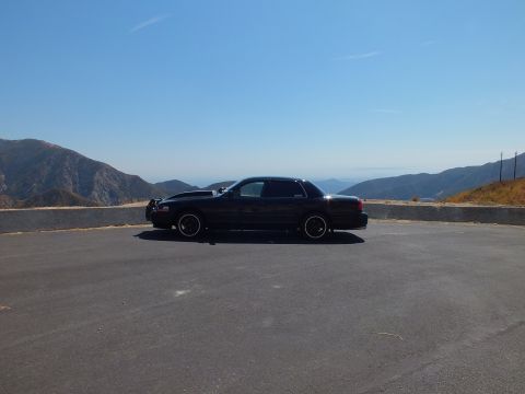 2003 Ford Crown Victoria - Lowered blacked-out Ford sedan parked across a wide overlook above hazy ridges
