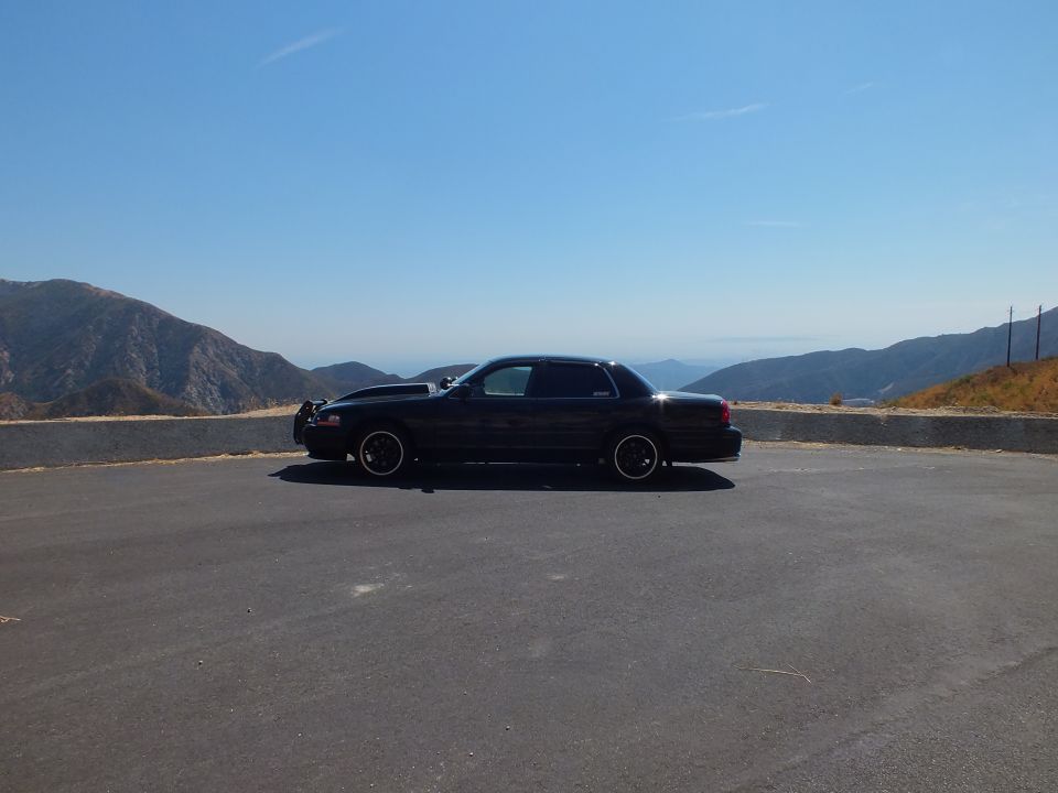 Black Crown Victoria sedan in profile on paved mountain pullout with valley vista
