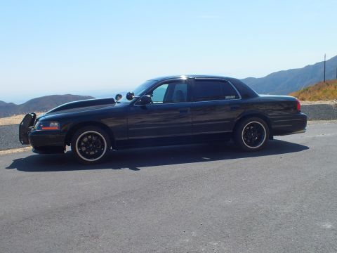 2003 Ford Crown Victoria - Lowered black Mercury sedan shown side-on with a front push bar, hazy peaks behind.