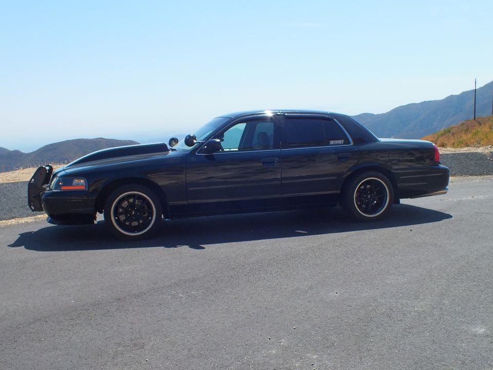 Black Mercury sedan side view with grille guard, black wheels, mountain road