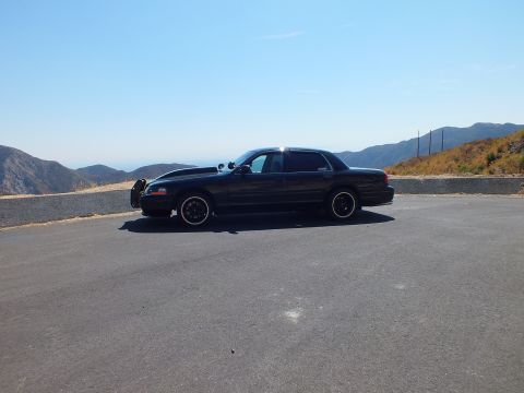 2003 Ford Crown Victoria - Wide profile of a blacked-out full-size sedan at a mountain turnout under clear sky.